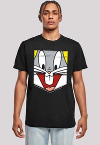 Černé bavlněné tričko s barevnou grafikou Bugs Bunnyho s usměvavým výrazem, umístěné na žlutém a bílém pozadí.