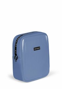 Harde reiskoffer in lichtblauw, met een geribde uitstraling, zwarte ritsaccenten en een logo patch aan de voorkant.