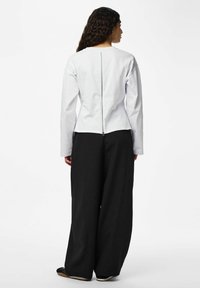 Haut blanc à manches longues avec un zip au dos, associé à un pantalon noir à jambes larges. Le tissu semble lisse et structuré.