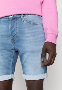 Bermuda in denim azzurro con risvolti, caratterizzata da una vestibilità standard, design a cinque tasche e dettagli di cucitura visibili.