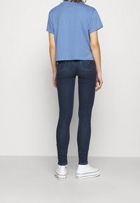 Avskuren blå t-shirt med korta ärmar, parat med mörkblå skinny jeans och vita sneakers. Viser en enkel, avslappnad outfit.