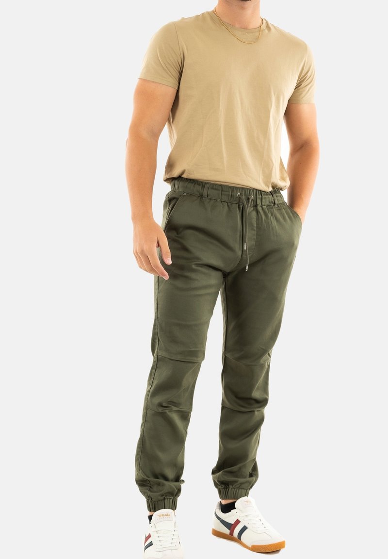 Olijfgroene joggers met een elastische tailleband en een trekkoord, taps toelopende benen en zijzakken. Draag ze met een aansluitend beige t-shirt en witte sneakers.