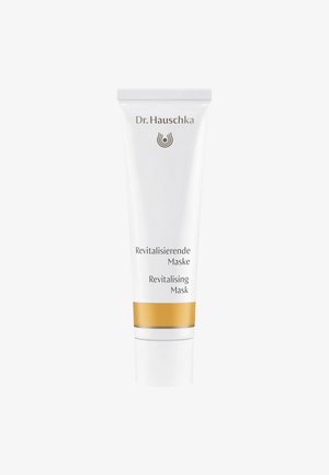 Tube en plastique blanc avec des accents dorés et argentés. L'étiquette présente "Dr. Hauschka" et "Masque Revitalisant" en texte noir. Design simple et épuré.