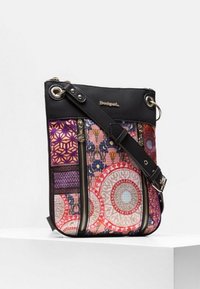 Crossbody bag with black top and adjustable strap, featuring colorful geometric and floral patterns and two vertical front zippers.