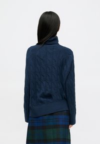 Pulover tricotat de culoare bleumarin, cu un model texturat de cabluri, guler înalt și tiv cu nervuri. Vedere din spate care arată un croi lejer și mâneci lungi.