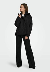 Czarna pikowana kurtka z kapturem, zapinana na guziki. Modelka ma na sobie czarne spodnie z szerokimi nogawkami, prezentujące casualowy styl.