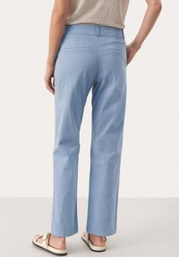 Lichtblauwe katoenen broek met een recht ontwerp, voorzien van achterzakken en een zoom die boven de enkel valt. Gecombineerd met lichte sandalen.