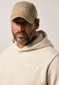 Cappello beige con ricamo "WOODLANDS EST. 1880"; felpa leggera beige con dettaglio in rilievo "MOTO COMPANY JP 1880". Colori neutri, stile casual.