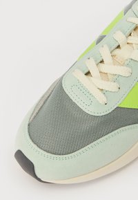 Sneaker featuring mint green and gray mesh, suede accents, cream laces, and a black rubber sole with a distinctive shape and design.