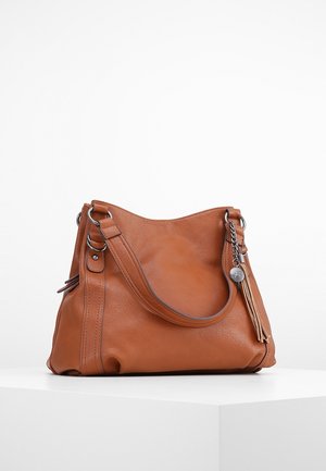 Sac à main en cuir marron avec ferrures argentées et breloque pompon attachée, posé sur une surface blanche sur un fond uni.