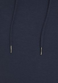Felpa blu navy in tessuto con superficie testurizzata, dotata di un cordino intrecciato e di terminali in metallo per una vestibilità regolabile.