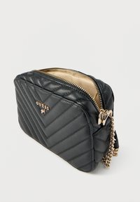 Musta tikattu synteettisestä nahasta valmistettu laukku, jossa kullanväriset metalliosat, vetoketjusuljin ja ketjuhihna. Sisäpuoli on beigeä kangasta.