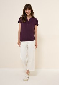 Fialový krátký rukáv top s henley výstřihem a knoflíkovými detaily, spárovaný s bílými širokými kalhotami a béžovými teniskami.