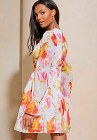 Rochie florală dintr-un material ușor, cu flori vibrante de culoare roșie, galbenă și roz, cu mâneci lungi și o fustă evazată care se termină deasupra genunchiului.