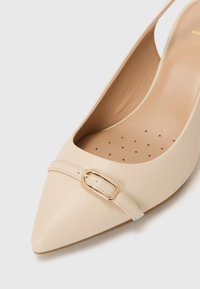 Scarpa slingback beige con punta affilata realizzata in pelle liscia, caratterizzata da una fibbia dorata e una soletta perforata per la ventilazione.