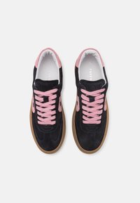 Baskets noires avec des détails en daim rose, lacets roses et semelles en caoutchouc marron, vues de dessus sur fond blanc.