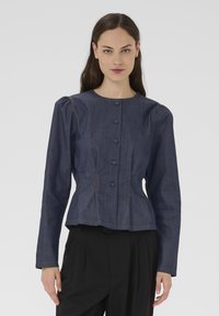 Giacca di jeans blu scuro con maniche lunghe, scollo rotondo e chiusura con bottoni. Caratterizzata da spalle imbottite e vita aderente a peplo.