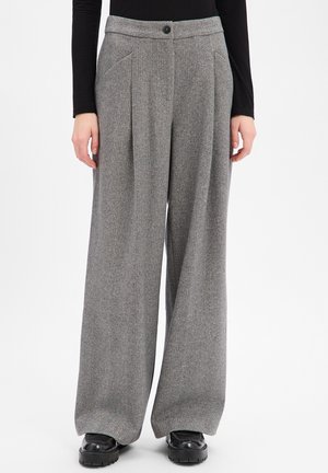 Pantalon gris à larges jambes en chevrons avec plis devant, poches latérales, fermeture par bouton, porté avec un haut noir à manches longues et des chaussures épaisses noires.