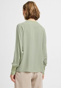 Maglia a maniche lunghe di colore verde chiaro con una finitura testurizzata e maniche raglan. Il capo ha un fit rilassato e un orlo posteriore allungato.