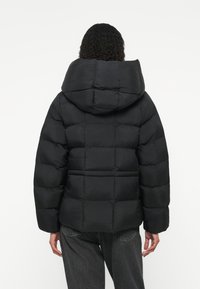 Čierna prešívaná bunda s kapucňou, s elastickými manžetami a skráteným strihom. Vyrobená z ľahkého a vodeodolného materiálu.