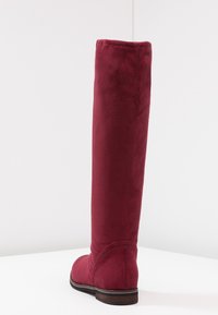Botte bordeaux en daim montant jusqu'au genou, avec une texture lisse, un embout arrondi et un talon en bois empilé. Design minimaliste sans éléments métalliques visibles.