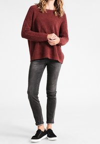 Bordeaux fluffig tröja med nedhasade axlar, tillsammans med mörka tajta jeans och svarta sneakers. Texturen verkar mjuk och mysig.