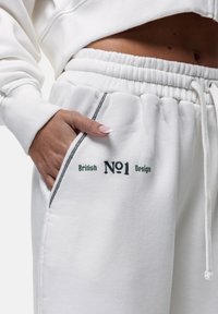 Witte sweatpants met een trekkoord in de taille, zijzakken en geborduurde tekst "British No1 Design" in groen en zwart.