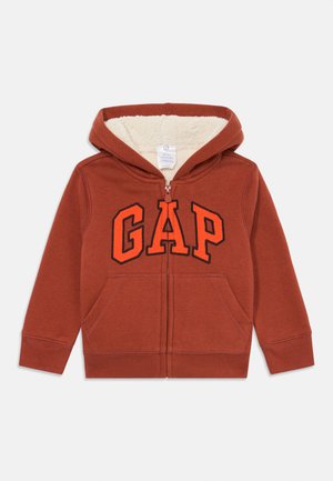 Roter Kapuzenpullover mit Reißverschluss und cremefarbener Fleece-Innenausstattung, mit einem auffälligen schwarzen und orangefarbenen "GAP"-Logo auf der Vorderseite und zwei Fronttaschen.