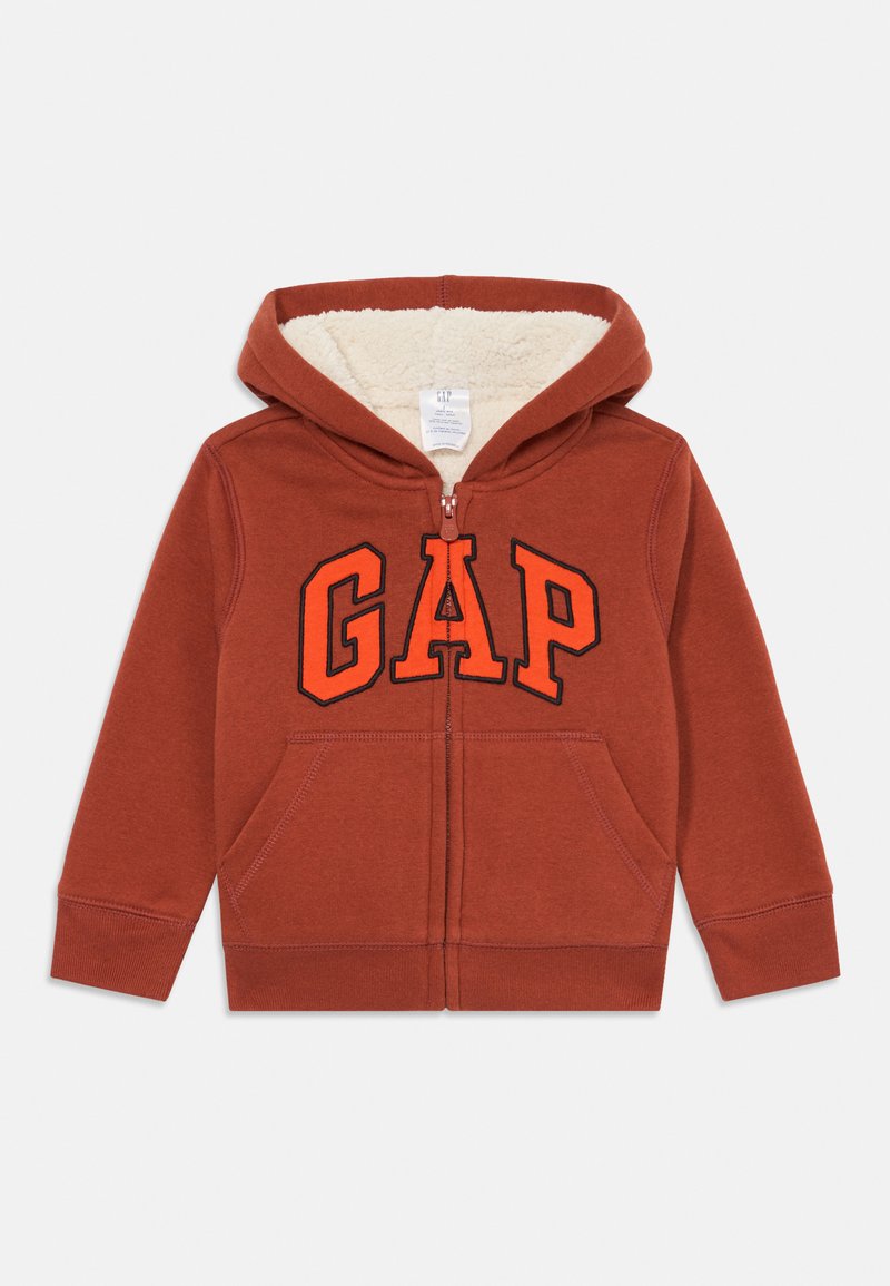 Rød zip-hoodie med kremfarget fleecefôr, med en dristig svart og oransje "GAP"-logo på forsiden og to lommer foran.