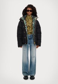 Doudoune noire avec doublure en imprimé animal vert, col roulé à motif, jean bleu délavé à jambes larges, et chaussures à plateforme noires.