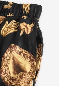 Pantaloni scurți din material negru, cu un motiv clasic auriu cu mâini, fețe și modele decorative. Talie elastică și buzunare laterale vizibile.