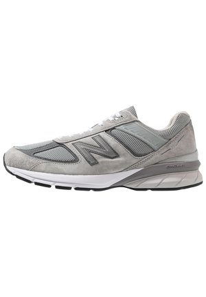 Grauer New Balance Sportschuh mit Mesh- und Wildlederpaneelen, weißer Zwischensohle, schwarzer Laufsohle und Schnürverschluss.