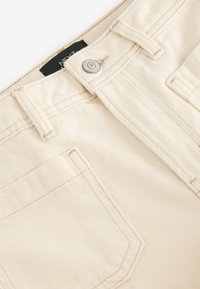 Beige katoenen broek met een klassieke vijf-pocketdesign, metalen knoopsluiting en subtiele verticale strepen in de stoftextuur.