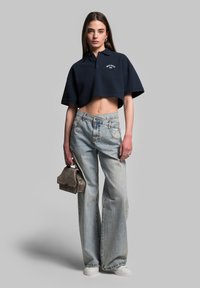 Granatowy krótki polo z logo, jasnoniebieskie, wyblakłe dżinsy z szerokimi nogawkami, szara mini torebka i białe sneakersy. Gładka tekstura, casualowy design.