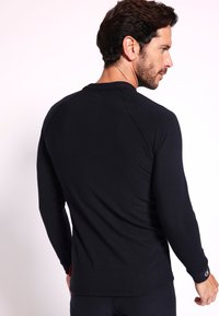 Schwarzes langärmeliges Shirt aus einem weichen Material. Verfügt über einen runden Halsausschnitt und Raglanärmel, mit subtilen Nähten und einem Logo-Detail.