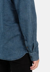Blauw gestreepte shirt met een knoopmanchet, voorzien van een zachte textuur en afgeronde zoom. Het materiaal lijkt lichtgewicht en casual in ontwerp.