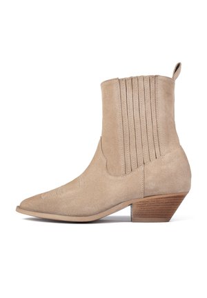 Bottine en suede beige avec un bout pointu, des détails nervurés sur la tige et un talon en bois empilé. Surpiqûres discrètes sur le bout.