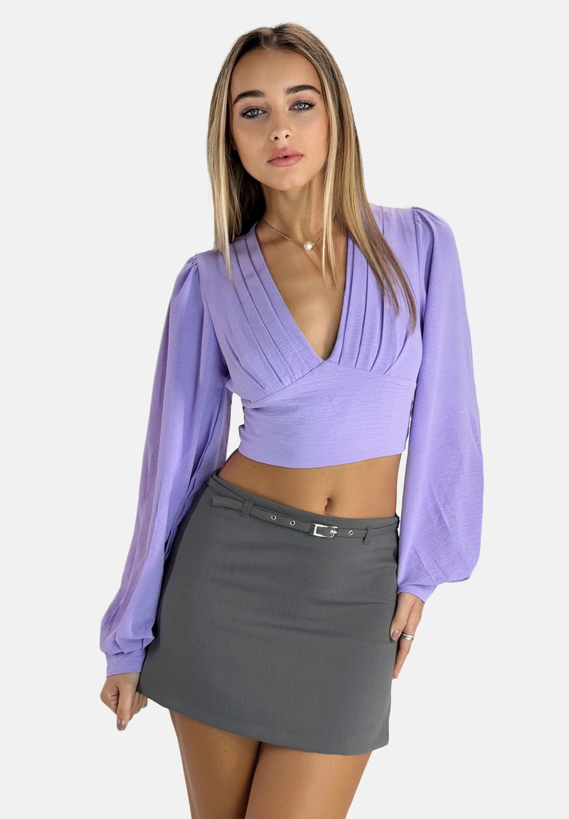Crop top lungo a maniche con design plissettato in lilla; abbinato a una minigonna grigia aderente con cintura e texture sottile.