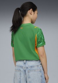 Camicetta a maniche corte verde e arancione con un motivo testurizzato sulle maniche; la scritta "CITY" stampata in arancione sulla schiena vicino al colletto.