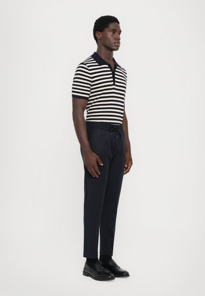 Camiseta polo de manga corta a rayas en navy y crema, con un cuello estructurado. Combinada con pantalones tapered navy y zapatos negros.
