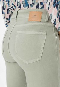 Hellgrüne Denim-Jeans mit zwei Gesäßtaschen, einem Lederetikett an der Taille und dekorativen Steppnähten. Der Stoff wirkt glatt und strukturiert.