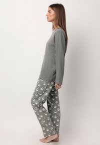 Camiseta de manga larga gris combinada con pantalones de pijama grises con patrones de calaveras sonrientes. Material de algodón con un corte holgado y textura suave.