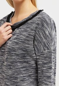 Gestrickter Pullover in Marineblau und Weiß mit einem strukturierten Muster, ausgestattet mit einem rohen Halsausschnitt und langen Ärmeln.
