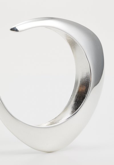 Sidabrinė metalinė apyrankė su elegantišku, lenktu dizainu. Ji turi lygią, blizgią paviršių ir siaurėjančią briauną, pabrėžiančią modernią formą.
