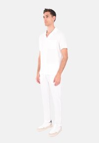 Camicia bianca a maniche corte con taschino, abbinata a pantaloni bianchi su misura e sneakers bianche. Tessuto semplice e liscio con una vestibilità rilassata.