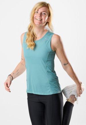 Lichtblauw, mouwloos sporttop met een gestructureerd patroon, gecombineerd met zwarte leggings. Onderwerp stretcht met een witte sneaker op de grond.