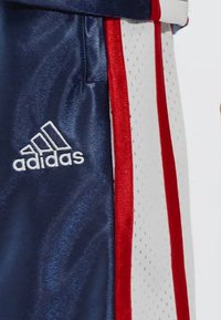 Calções atléticos azul-marinho com riscas laterais vermelhas e brancas, feitos de um tecido suave, com um logo Adidas bordado em branco.