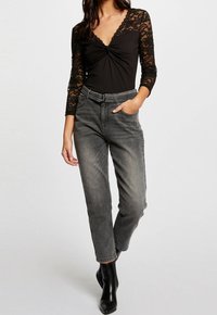 Body in pizzo nero a maniche lunghe con design incrociato davanti, abbinato a jeans in denim grigio scuro a vita alta e stivaletti neri.
