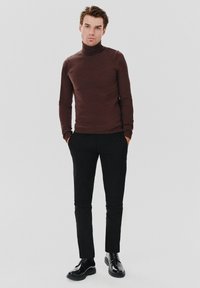 Brązowy sweter z kołnierzem typu golf, wykonany z gładkiego materiału, w połączeniu z czarnymi spodniami slim-fit i błyszczącymi czarnymi butami na sznurówki.