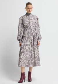 Vestido de estampado floral en tonos de púrpura y crema, con un escote alto, mangas largas, una cintura fruncida y una silueta fluida.